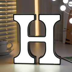 the illuminated letter h sits next to a coffee cup and cell phone on a table