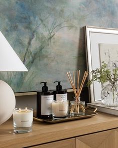 candles on a tray next to a painting and framed artwork in front of a wooden dresser