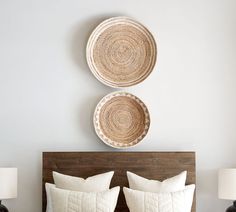 two baskets are hanging on the wall above a bed with white linens and pillows