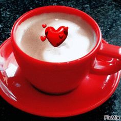 a red cup filled with liquid and a heart shaped decoration on the top, sitting on a saucer