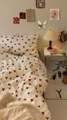 a bed with white sheets and red hearts on it, next to a small table