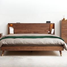 a bed with two nightstands next to it in a white walled room and a green blanket on the bed