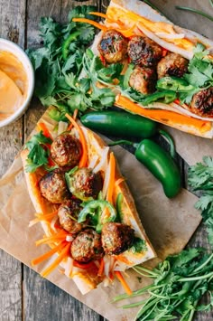 two sandwiches with meatballs, carrots and lettuce next to dipping sauce