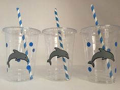 three plastic cups with blue and white striped straws in front of dolphins on them