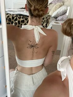 a woman with a dragonfly tattoo on her back is looking at herself in the mirror