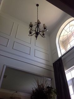 a chandelier hanging from the ceiling in a room with two windows and a potted plant