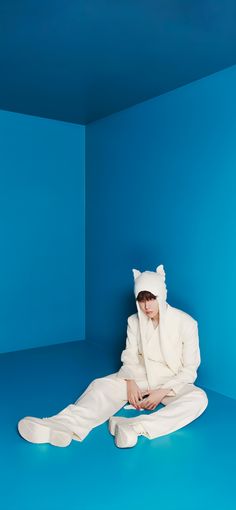 a person sitting on the ground wearing a white cat suit and matching shoes with a blue background