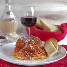 a plate with spaghetti and meatballs on it next to a glass of red wine