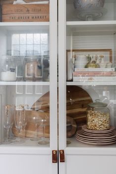 the shelves are filled with dishes, glasses and other kitchen items in glass fronted cupboards