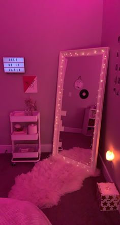 a pink room with a mirror and lights on the wall, next to a bed