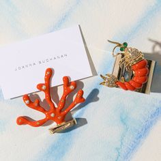 an orange coral shaped brooch sits next to a white card