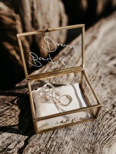 an open box with two wedding rings in it sitting on a piece of drift wood