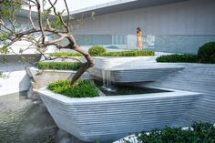 a woman standing in front of a building next to a tree with water flowing from it