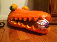 an orange pumpkin shaped like a alligator with its mouth open and teeth wide open, sitting on a wooden floor