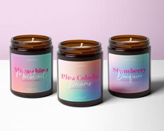 three candles sitting next to each other on top of a white table with a pink and blue background