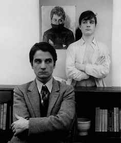 black and white photograph of man sitting in front of bookshelf with his arms crossed