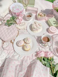 a table topped with cupcakes and cakes next to pink flowers on top of a blanket