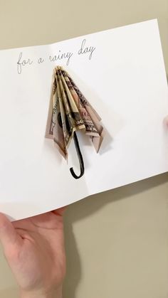 someone holding up a card with an umbrella made out of money and the words for a rainy day written on it