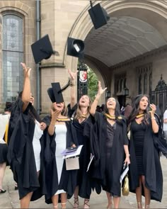 graduates throwing their caps in the air on graduation day outside an old building with arched doorways