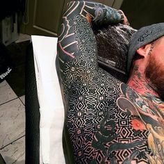 a man with tattoos on his arm and chest laying down next to a white counter