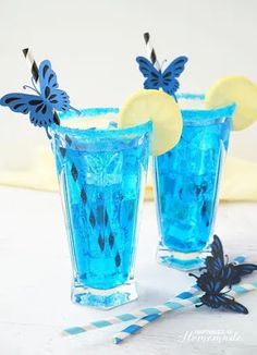 two glasses filled with blue liquid and topped with lemon slices, butterfly straws and paper straws