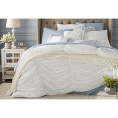 a bed with white and blue comforters in a room next to a lamp on a table