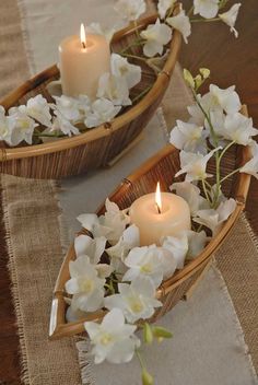 two baskets filled with white flowers and lit candles on top of a cloth covered table