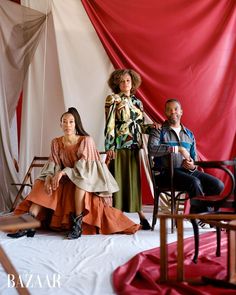 three people sitting on chairs in front of red and white drapes with one person standing up