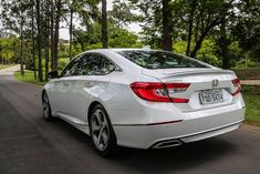 the rear end of a white car driving down a road with trees in the background