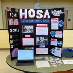 a table with a laptop on top of it in front of a sign that says hosa