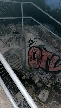 graffiti on the side of a concrete wall near some metal bars and railings at night