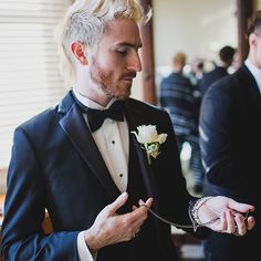 a man in a tuxedo adjusts his boutonniere as another man looks on