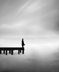 a man standing on top of a pier in the middle of foggy water with his back to the camera