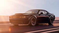 a black sports car driving on the road at sunset or sunrise with its hood down