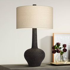 a table with a lamp and vase on it next to a framed photograph, flowers and a painting