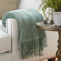 a white chair with a green blanket on top of it next to a potted plant