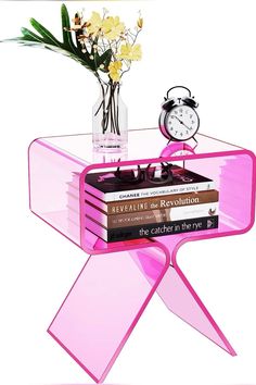 there is a pink table with books and a vase filled with flowers next to an alarm clock