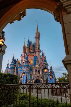 the entrance to disneyland's castle is shown through an arched gate at dusk with lights on