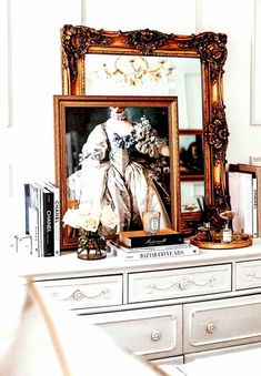 a white dresser topped with books and a framed photo next to a vase filled with flowers