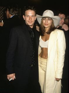 a man standing next to a woman in a white suit and hat at an event