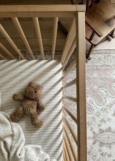 a teddy bear laying on top of a bed next to a wooden table and chair