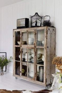 an old wooden cabinet with glass doors in a room filled with plants and other items