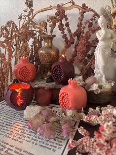 pomegranates and flowers on display in front of a book with an angel statue