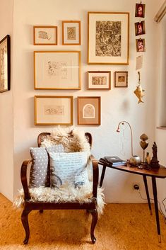 a living room filled with lots of framed pictures on the wall above a chair and table