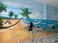 a person painting a mural on the wall in a room with palm trees and water