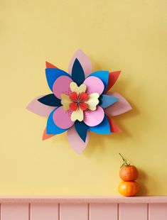 a paper flower sitting on top of a pink shelf next to an orange and yellow wall