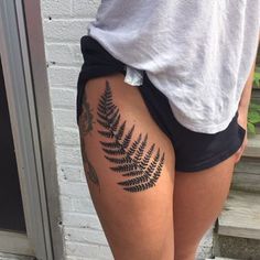 a woman with a tattoo on her thigh shows off her black and grey fern - print shorts