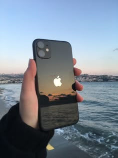 someone is holding up their iphone in front of the ocean at sunset or sunrise with an apple logo on it