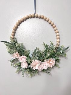 a wooden beaded wreath with flowers and greenery hangs on the wall in front of a white wall