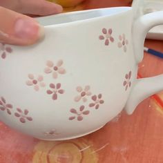 a person is holding a white coffee cup with pink flowers painted on the outside and inside